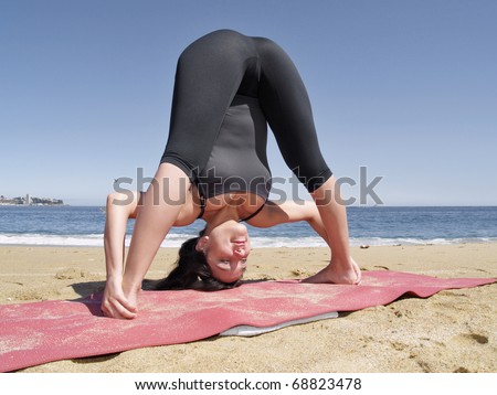 Yoga teacher practising at the beach pose dandayamana bibhaktapada pashimottanasana