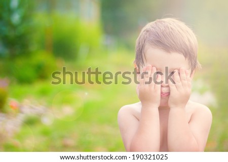 little child is playing hide-and-seek hiding face in sunlight with boke