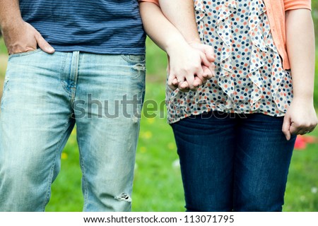 Young happy couple holding hands show at waist height showing their jeans and the womans diamond engagement ring.