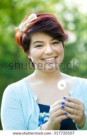 Attractive young brunette woman under soft natural lighting blowing flower petals from her hands. Shallow depth of field.