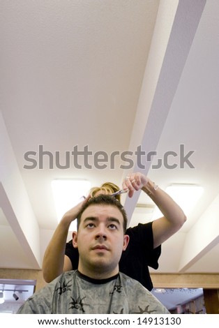 A young man getting his hair cut by a hairdresser at the beauty salon.  Plenty of copy space with this unique perspective.