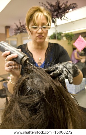 A hairdresser applying hair color to a clients head.  Shallow depth of field with focus on the hair.