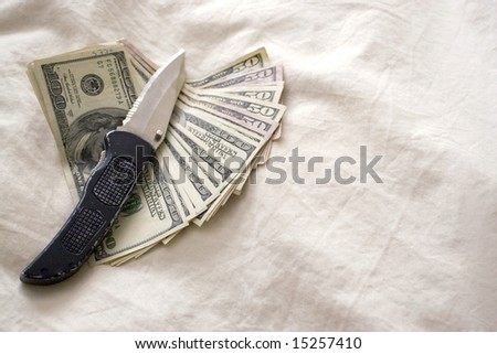 A knife and some fanned out cash laying on a bed.
