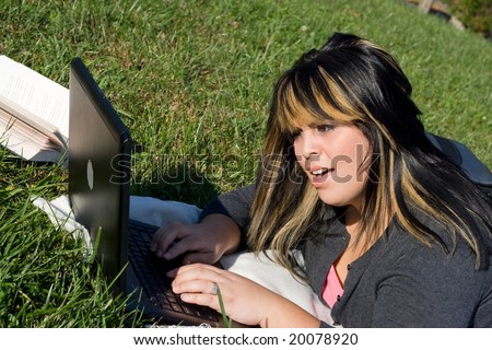 A young student surprised or disgusted by something she\'s seeing on her social media websites while laying in the grass on a nice day.