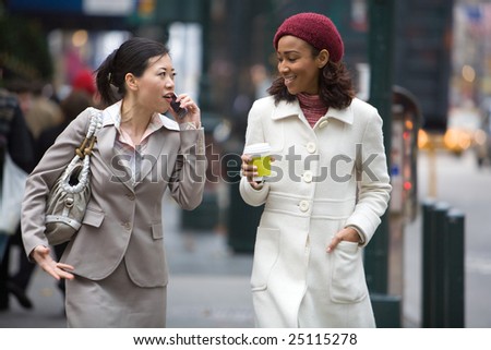 Two business women walking in the big city. One is on her cell phone.