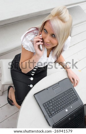 A beautiful young blond woman in a mobile business setting with her cell phone and laptop.