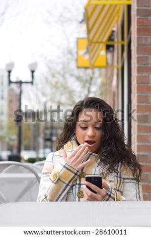 An attractive Indian woman texting or searching the web on her cell phone while seated at a table outdoors.