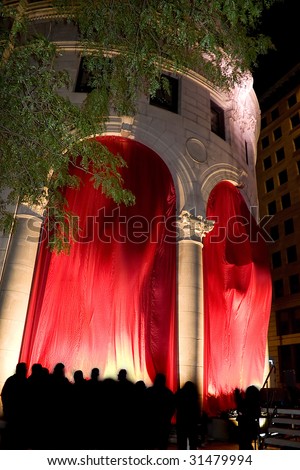 Classic architecture with flowing red curtains.  The silhouettes of the crowd are seen all around.