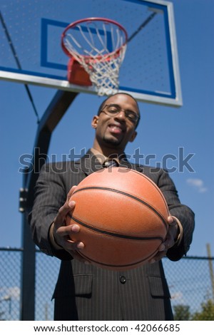 A young man in a business suit posing with a basketball.  He could be a coach player recruiter scout or trainer. Shallow depth of field with focus on the ball.