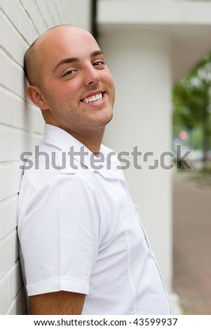 A young man with a casual pose leaning against a brick wall.