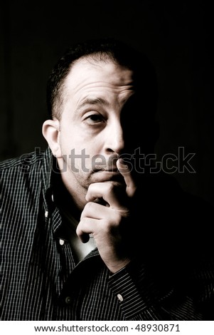 High contrast portrait of a middle aged man with a contemplative look on his face.  He could be worried or anxious about something on his mind.