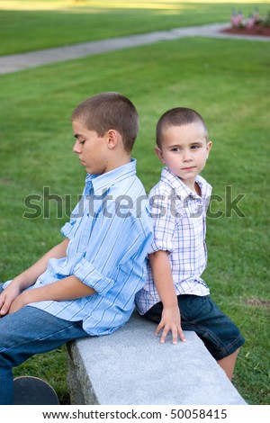 Two brothers sitting back to back on a bench in the park.