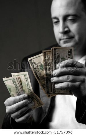 A crooked looking man counting a handful of one hundred dollar bills. Shallow depth of field.