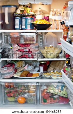 An open refrigerator door showing a full stocked fridge loaded up with food and fresh ingredients.