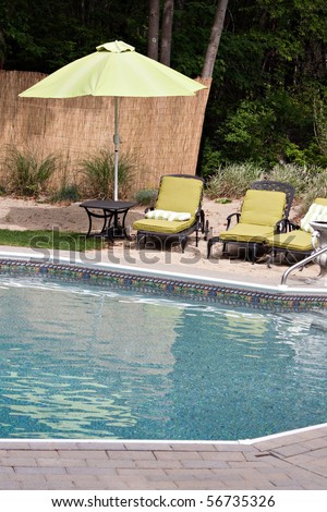 Detail view of a luxurious in ground swimming pool and patio lounge.  This partly wooded backyard garden offers the same level of luxury found in many vacation resorts.