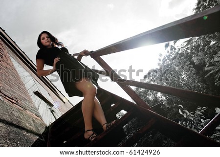 A young lady poses on a rusted old stairway in an urban setting with lens flare.  Selective color.