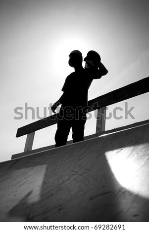 Silhouette of a young teenage skateboarder at the top of the half pipe ramp at the skate park.