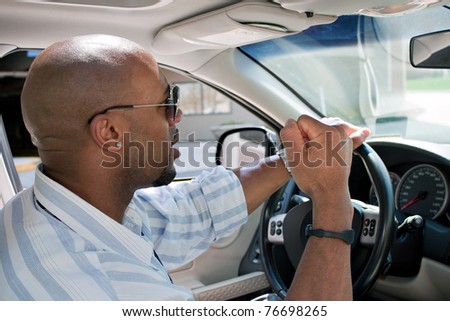 An irritated man driving a car is expressing his road rage with his fist clenched in the air.