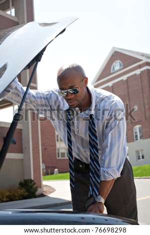 A business man having a bad day checks under the hood of his car to figure out what the problem is.