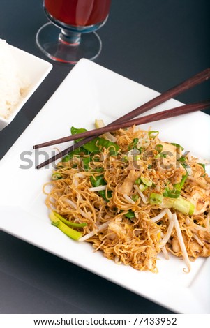 A Thai dish of stir fried chicken vegetables noodles jasmine rice and bean sprouts on a large white plate with chop sticks.