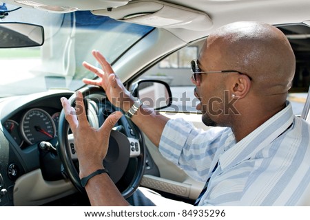 An irritated business man driving a car is expressing his road rage with his hands in the air.