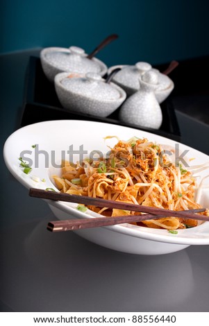 A Thai dish of crispy noodles and bean sprouts in a large white bowl with chop sticks.