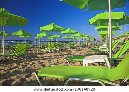 Many green umbrellas and folding beds on the sandy seashore. Abandoned beach.
