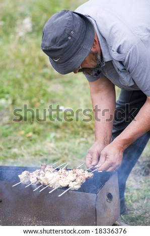The man fries a kebab on open fire. Picnic on the nature