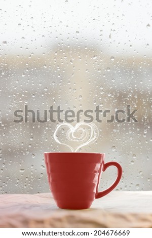 Steaming coffee cup on a rainy day window background with heart shape