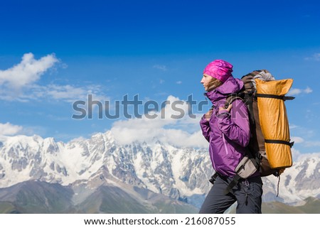 happy girl with a backpack and beautiful snowy summer landscape on background. travel sport lifestyle concept