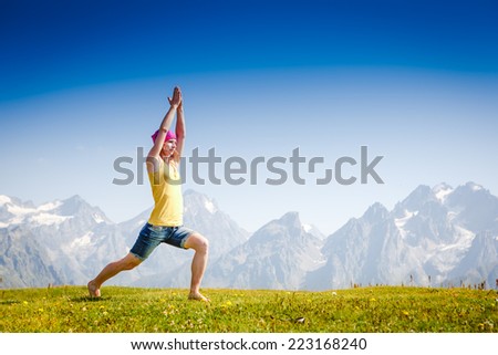 Young woman in warrior yoga pose standing on the grass under beautiful cloudy sky