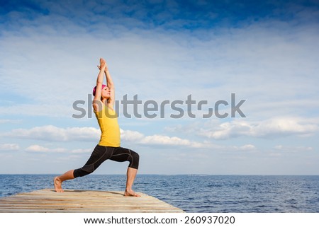 Woman practicing yoga outdoors over blue sky background