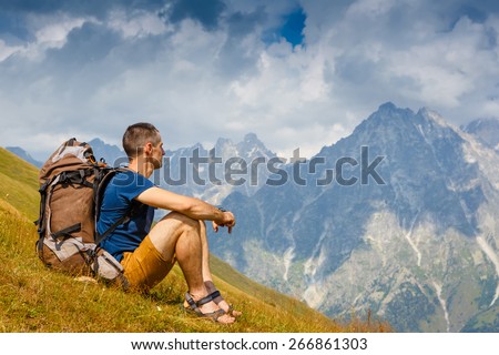 Hikers with backpack sitting on the grass in the mountain and looking into the distance