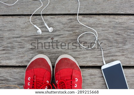 red sneakers and tablet with white headphones on wooden floor background
