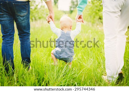 Portrait of a happy young family teaching baby to walk in the park
