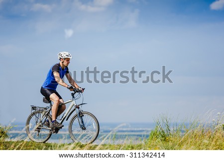 Young man cycling on a rural road through green spring meadow