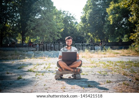 young stylish man using notebook at the park