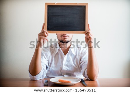 young stylish man with white shirt holding blackboard behind a table