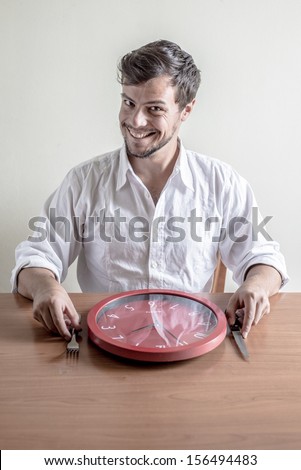 young stylish man with white shirt eating red clock behind a table