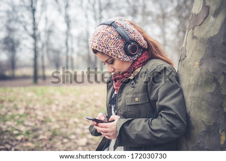 beautiful brunette woman listening to music with headphones at the park outdoor in winter