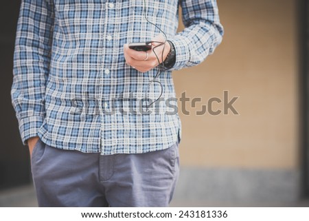 handsome hipster casual multitasking modern man listening music and using smartphone in the city