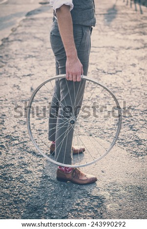 close up of legs shoes hipster man holding old bicycle wheel in the city