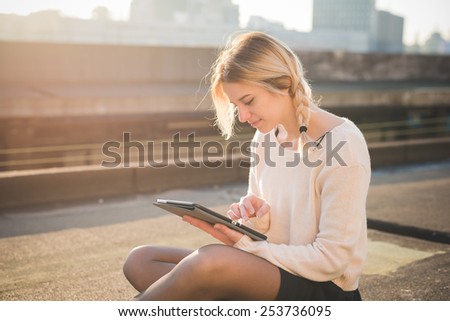 young beautiful blonde woman outdoor in the street of the city using technological device tablet connected online wireless sitting in the ground