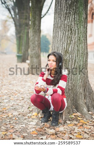 young beautiful indian woman at the park in autumn listening music with headphones