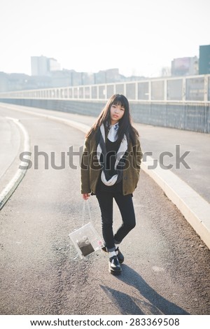 young beautiful asian hipster woman in the city - living town during sunset in backlit