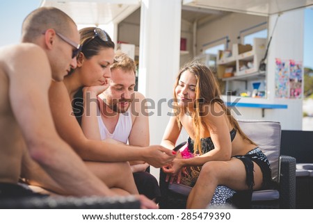 group of young multiethnic friends women and men at the beach bar in summertime using smartphone