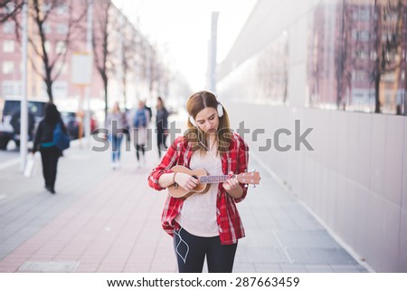 young beautiful blonde hipster woman in the city with ukulele and headphones