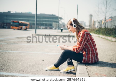 young beautiful blonde hipster woman in the city listening to music with headphones and smartphone