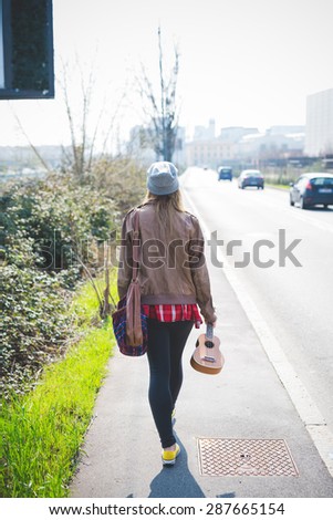young beautiful blonde hipster woman in the city road with ukulele