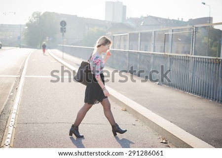 Young and beautiful blonde caucasian girl jaywalking, wearing a blu and pink floral dress with black skirt.